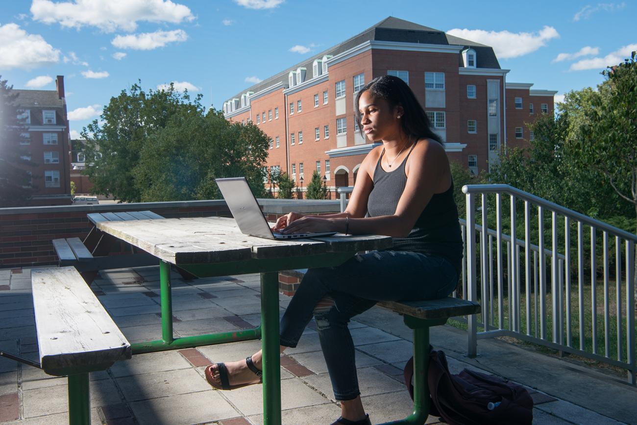 Woman sitting at a laptop on a picnic table outdoors