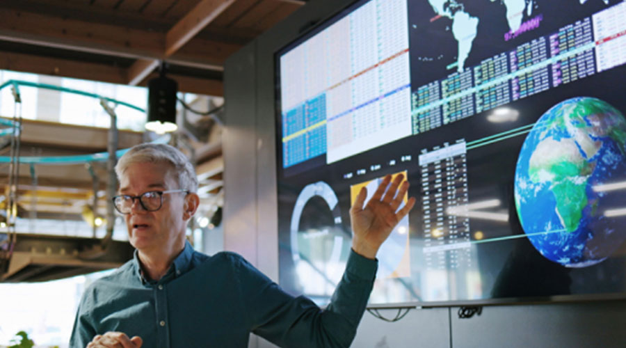 Man at screen pointing to map of the world with charts 