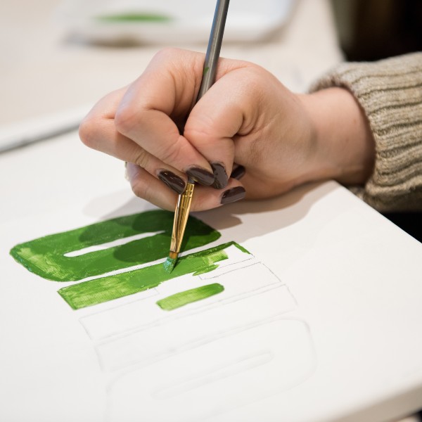 Close up on hand holding paintbrush painting OHIO in green on white canvas