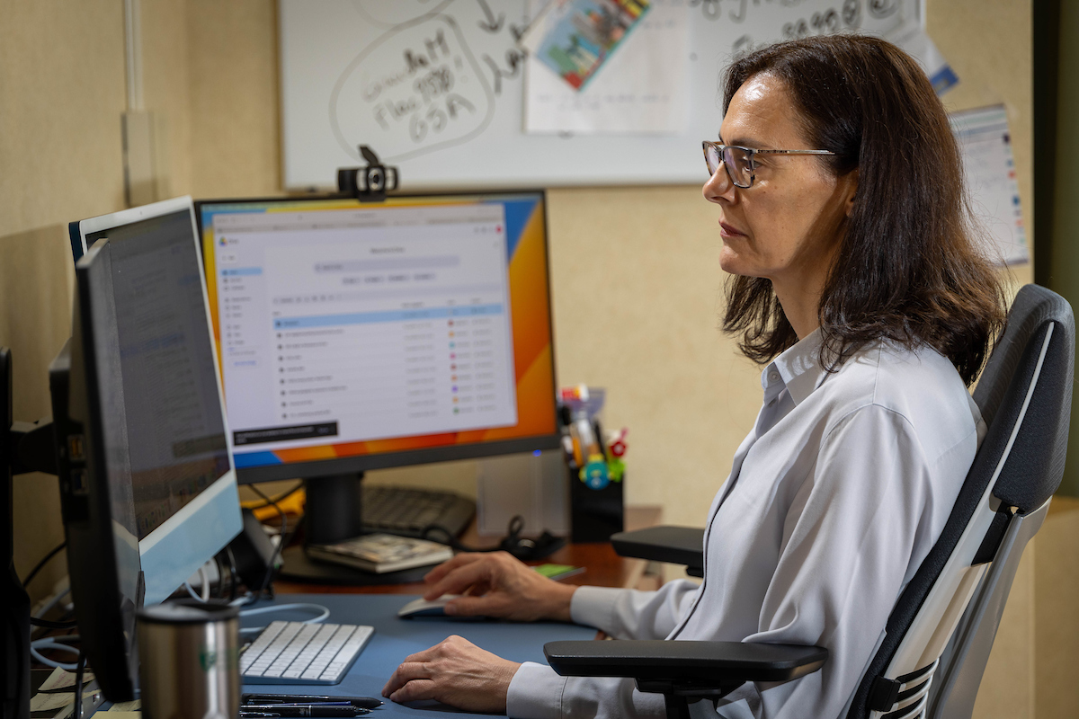 woman working at her desk, looking at two computer monitors