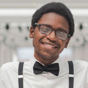 Charles Sanders smiles at the camera, wearing a white shirt and black suspenders and a bowtie.