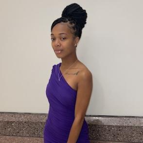 Dèja Pulley stands with one shoulder toward the camera, wearing a one shoulder purple dress.