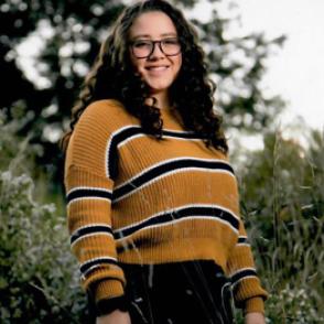 Hannah Prante smiles at the camera, wearing a yellow sweater with thick horizontal black stripes bordered by thinner white stripes
