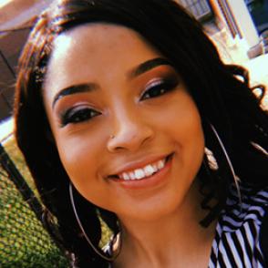 Makayla Moore smiles at the camera in a selfie photo, wearing gold hoops and a black and white vertically striped blouse