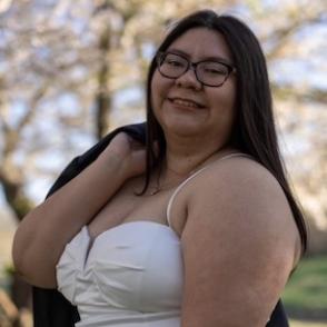 Maribel Antunez-Uriostegui stands in a white dress, a graduation gown draped over one shoulder.