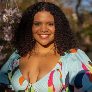 Maya Meade smiles at the camera, wearing a pale blue dress with some streaks of colors.