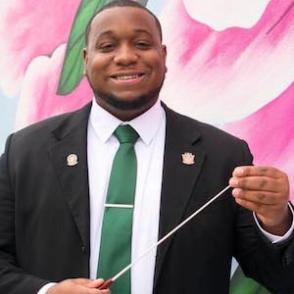 Nicholas Jarelle Cannady holds a conductor baton, wearing a black blazer and white shirt, with a green tie.