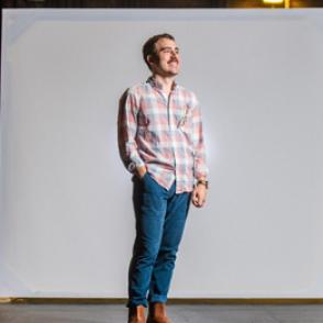 Roberto Di Donato stands in a studio, with one hand in a pocket, wearing jeans and a plaid shirt