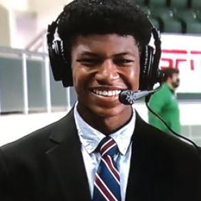 Sedric Granger, Jr. wears a black suit with a navy, dark red and white striped tie. Sedric wears a broadcaster headset.