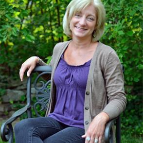 Valerie J. Allen sits in a chair in front of plants, smiling at the camera.