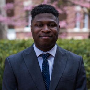 Vincent Eguakun wears a dark gray suit and a dark blue tie, half-smiling at the camera