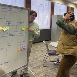 four colleagues looking a white board, trying to solve a problem