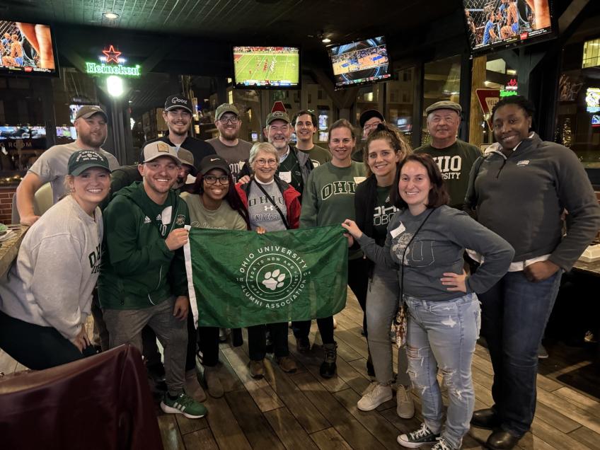 Group photo of OHIO grads holding green flag with OUAA logo.