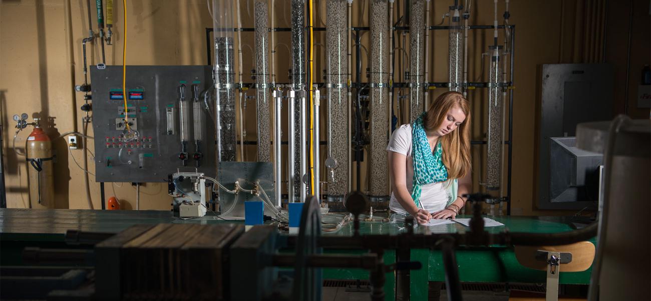 Female student standing at desk in front of tubes and dials