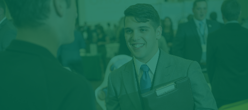 A student in a suit converses with an employer at a career fair. 