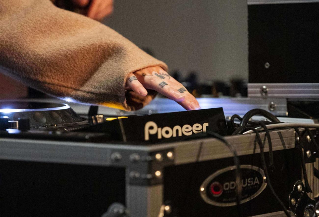 Hand with tattoos turning knobs on DJ sound board
