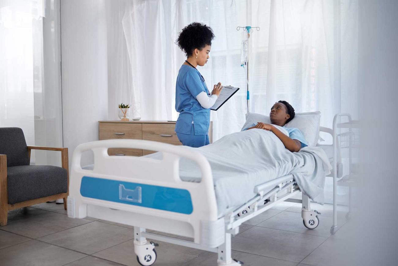 Nurse standing beside patient bed holding a clipboard