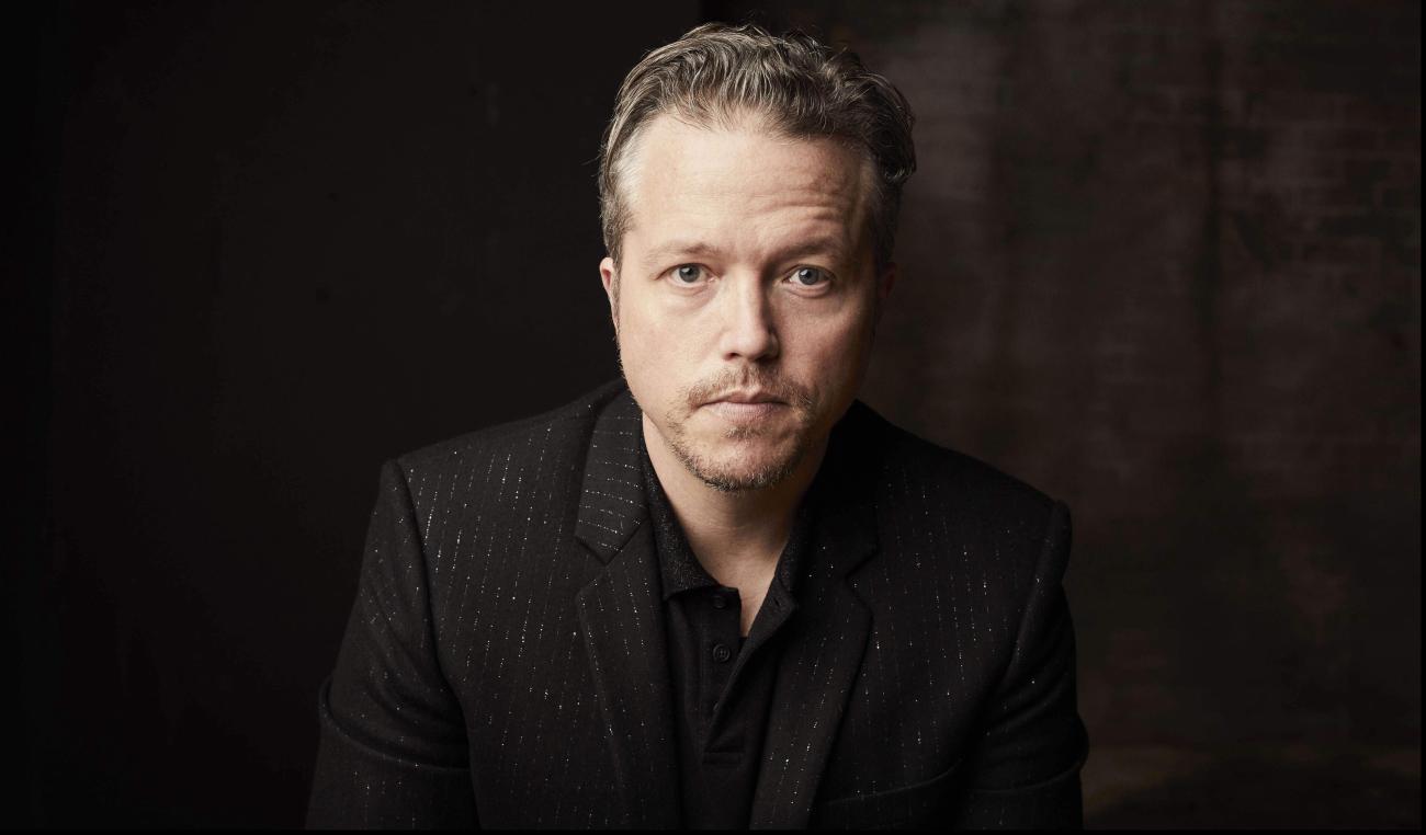 Jason Isbell with black jacket on looking into camera with black backgroung