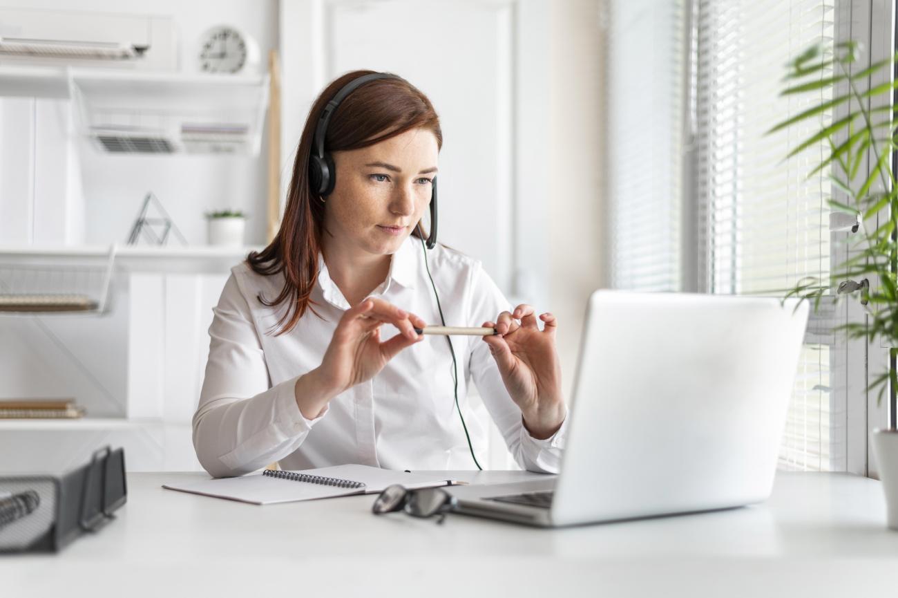 A woman looking at her computer with headphones on. Image by Freepik.