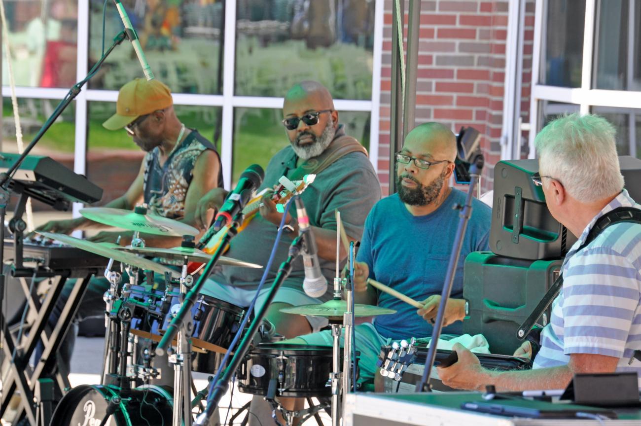 Four men playing drums, guitar, and keyboard