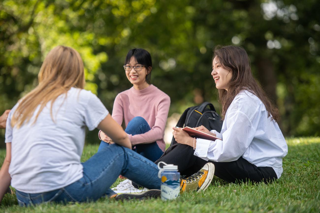 Three international students sitting on grass together