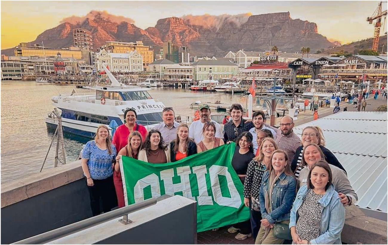 Group photo holding up OHIO green flag with water and boats in background.