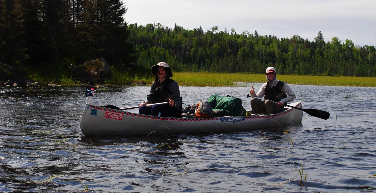 2 students paddling canoes in the water. 