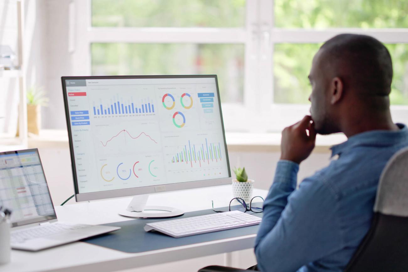 Man in blue shirt at desk looking at charts on monitor