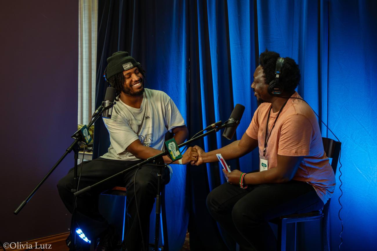 Two people shaking hands while wearing headphones and speaking into microphones