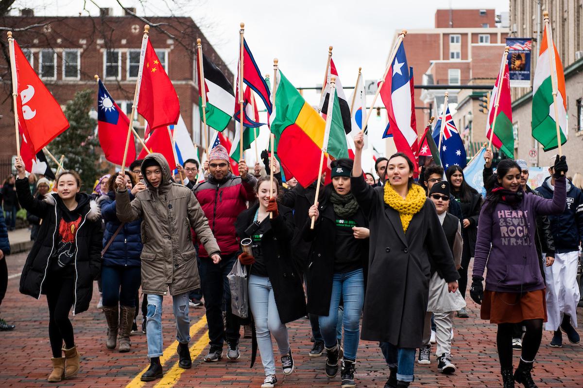 A group of people standing in a parade, with a variety of different countries' flags