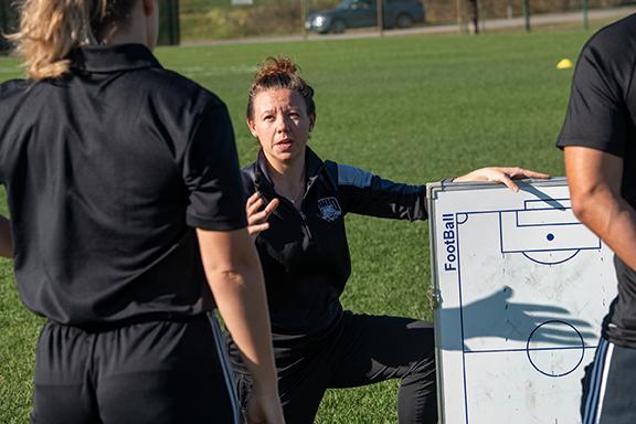 woman coach kneeling with a whiteboard in front of two soccer players