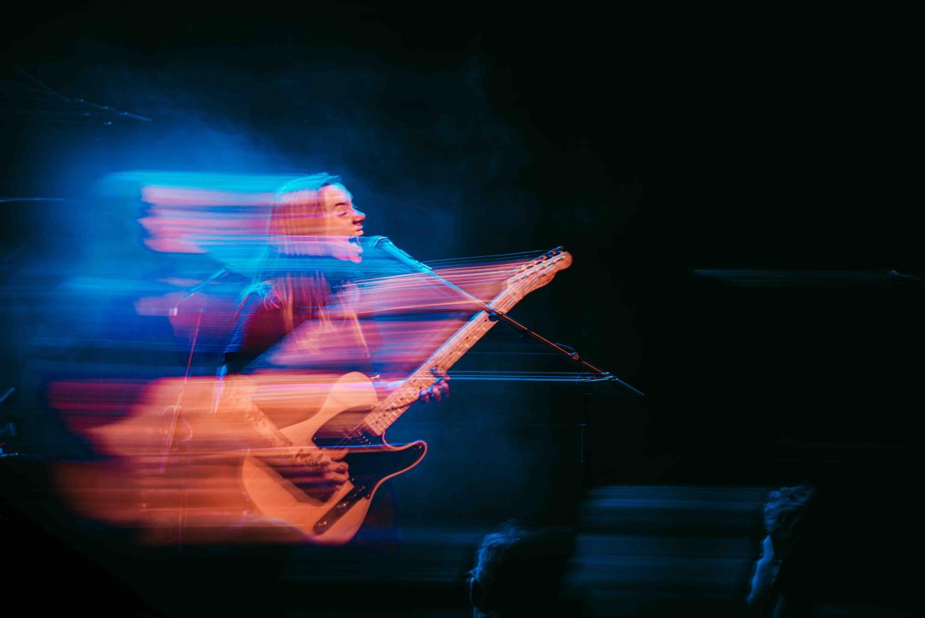 Julien Baker playing guitar and singing into microphone with blue effect on image