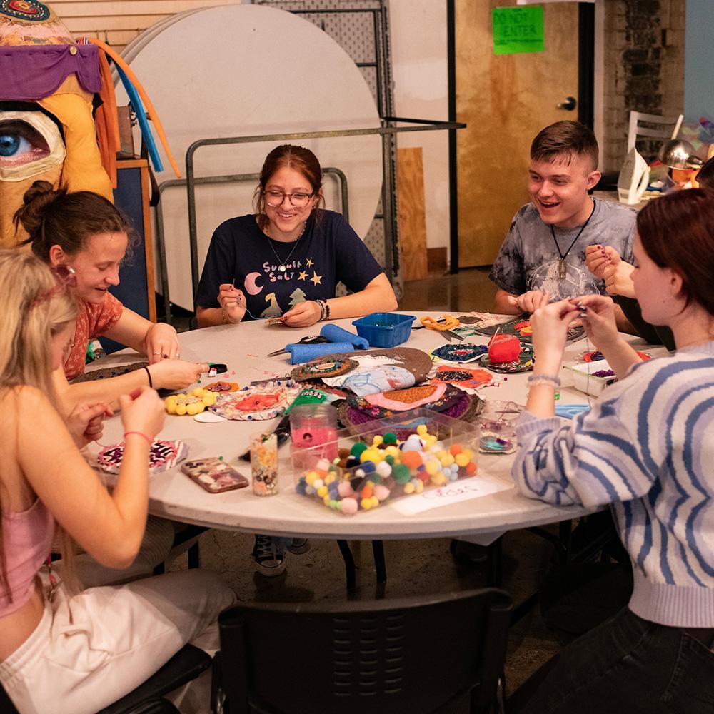 Students smile while sitting around a table of crafts