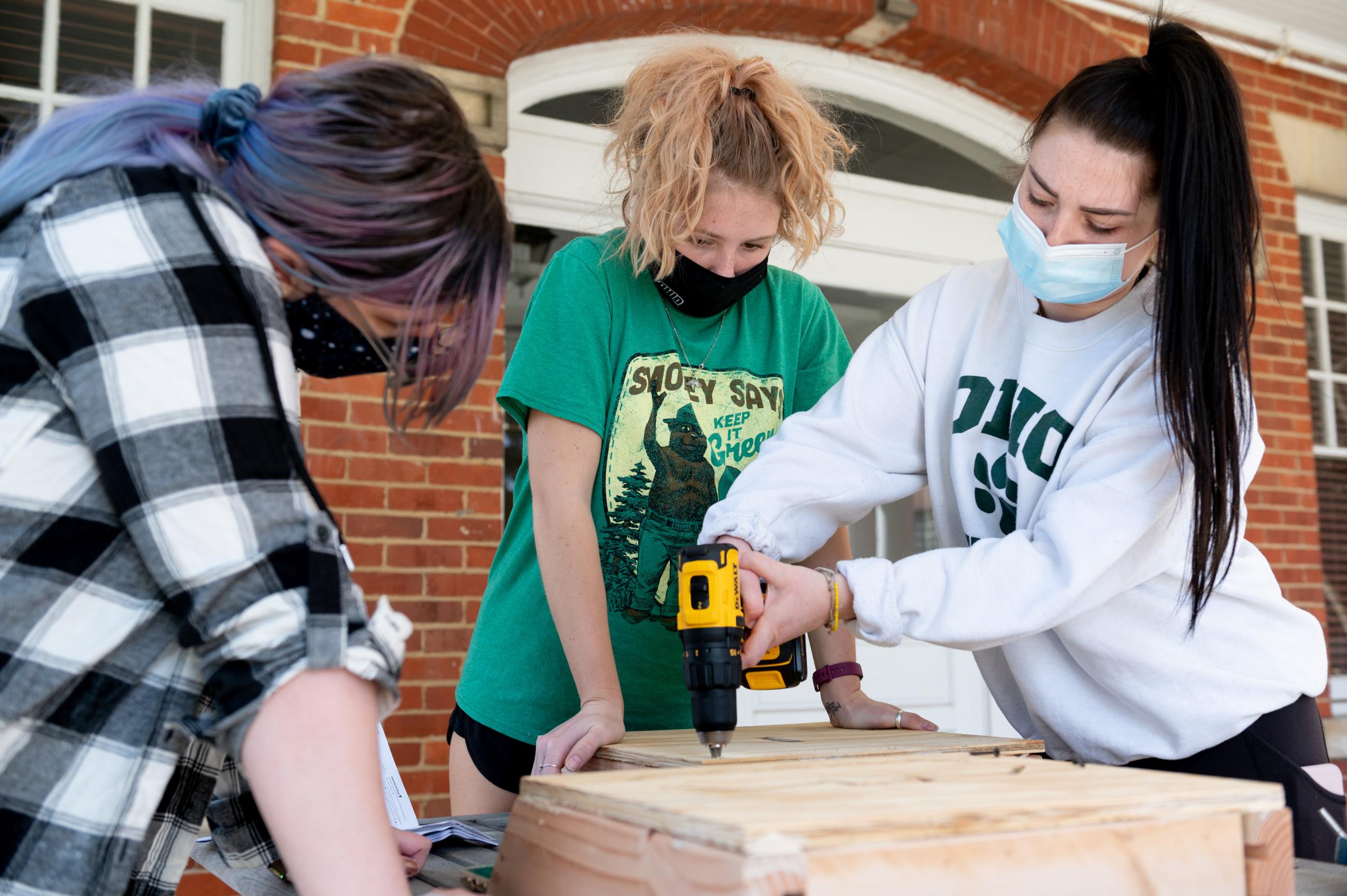 Three woman use a power drill to build a bat house.