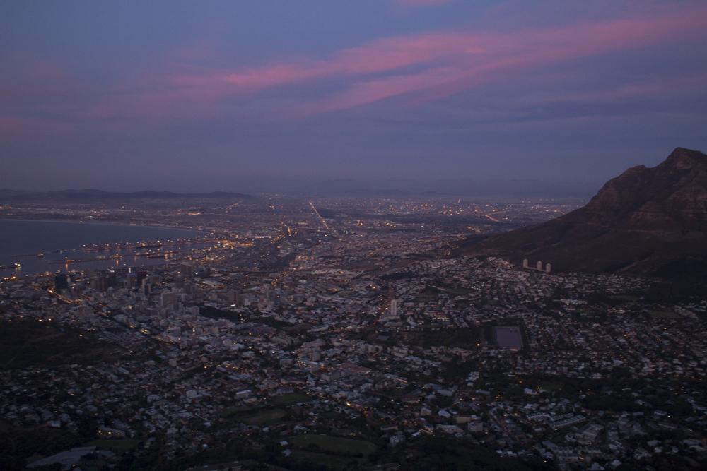 View over Cape Town at night. Lights from the city are visible with water on the left and mountains on the right side of the photo.