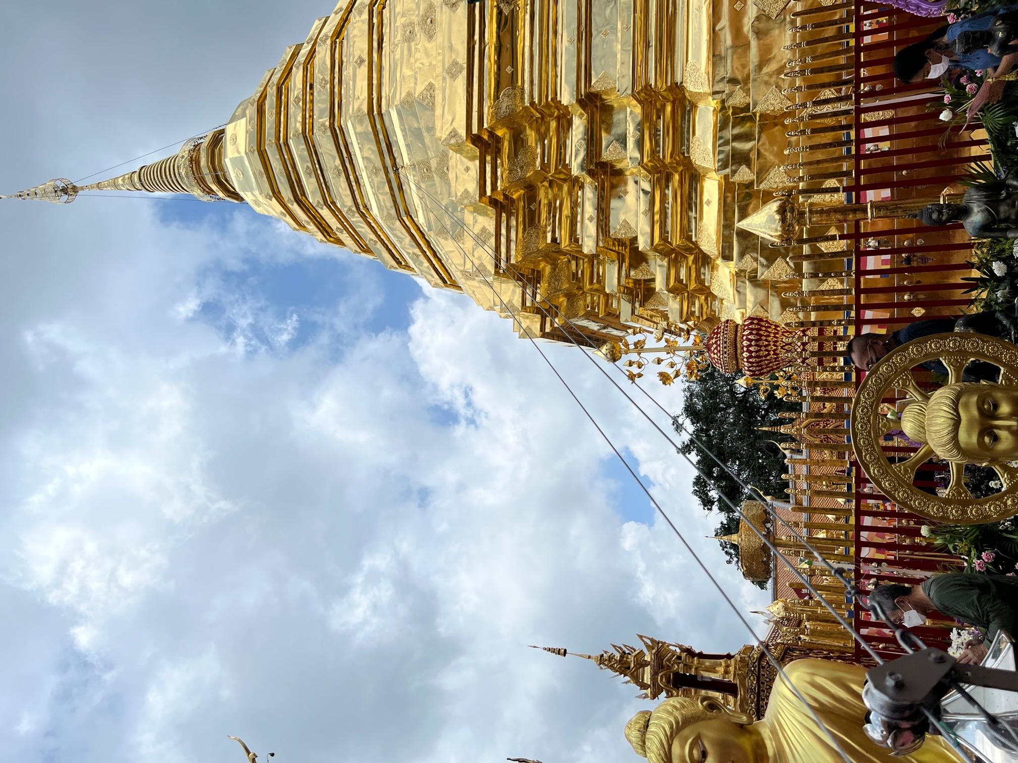 A golden and heavily ornate temple with statues of Buddha in the foreground