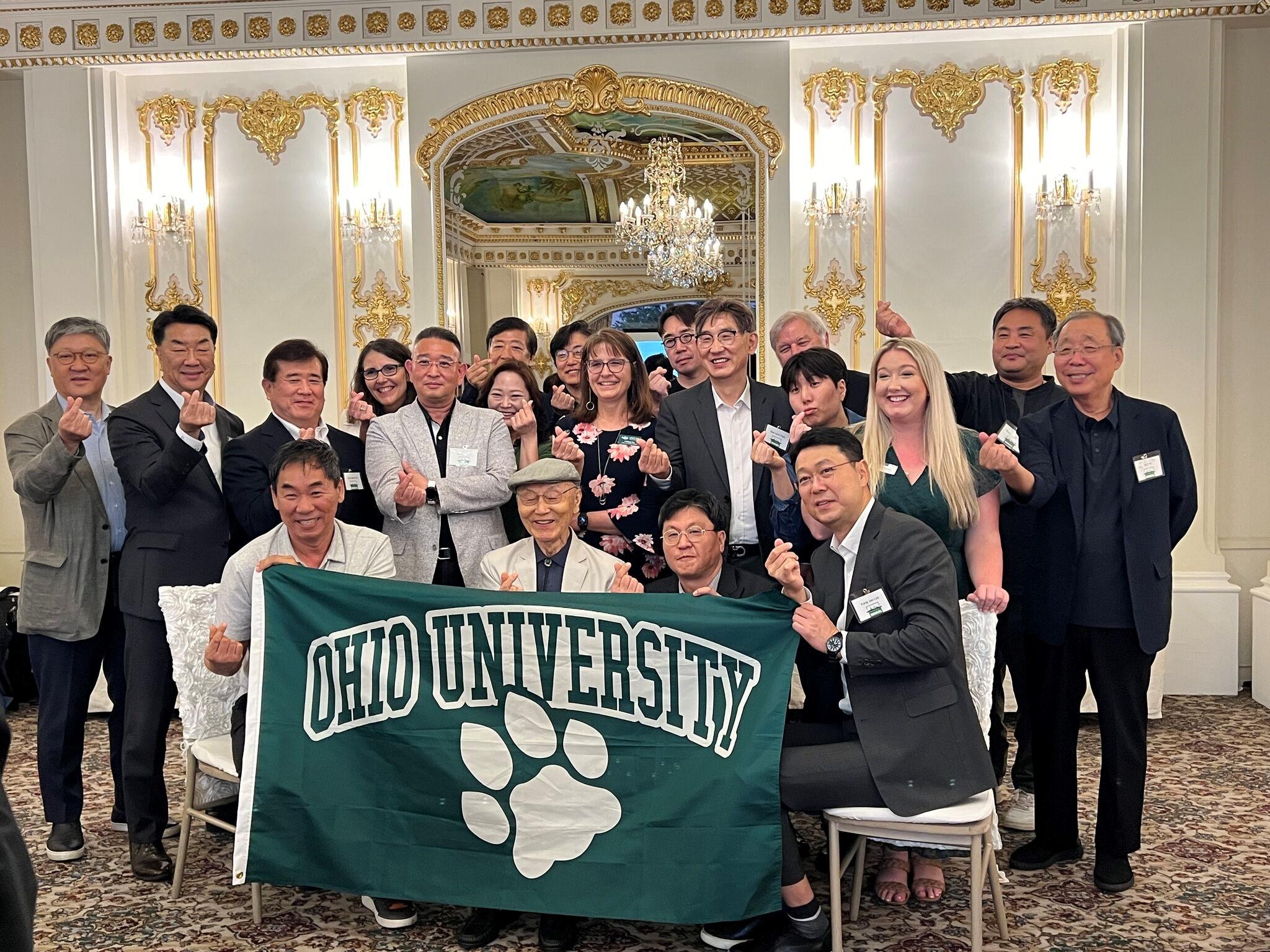 Group photo holding up green Ohio University flag with paw print.