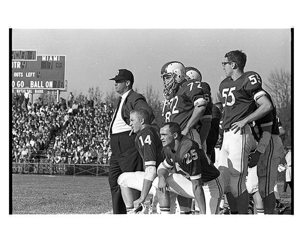 Former Ohio University Bobcats coach Bill Hess walks with some football players on the football field.