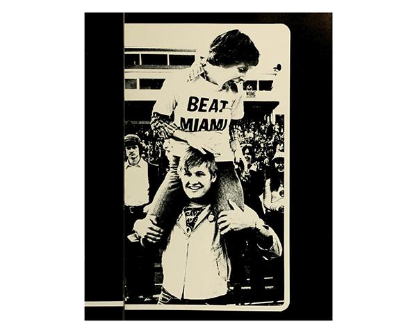 A student wearing a "Beat Miami" shirt sits atop another student's shoulders. 