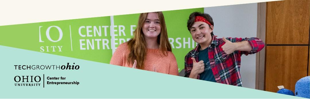 Two students giving thumbs up signs in front of Entrepreneurship Center window