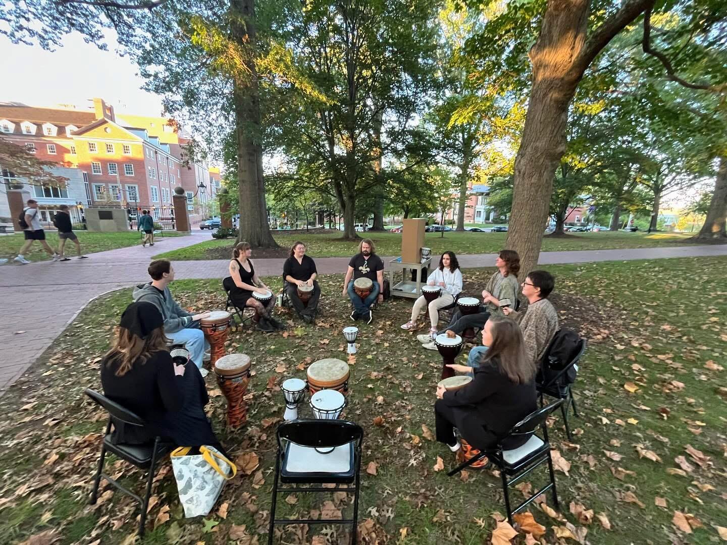 Students sit in a drum circle outside on College Green