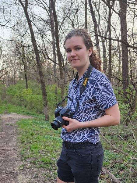 Pearl Schafer holding a camera in an outdoor environment with trees behind. 