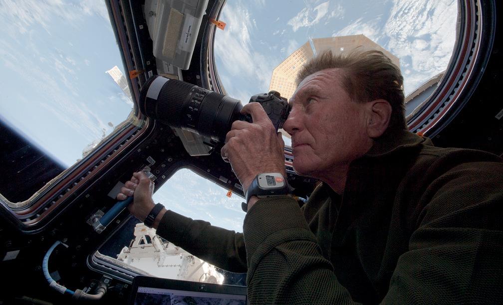A man on a space capsule holds up a camera and takes photos of Earth from space.