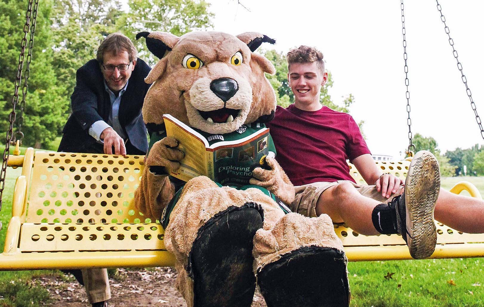 Mark Shatz and his son, Ethan Shatz, a first year, take a swing with Rufus as he studies the finer points of psychology. Photo by Ellee Achten, BSJ ’14, MA ’17