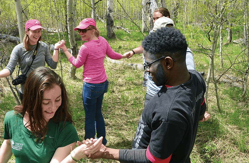 Students celebrate completing a "human knot" challenge in an aspen grove near the TSS Kelly Campus.