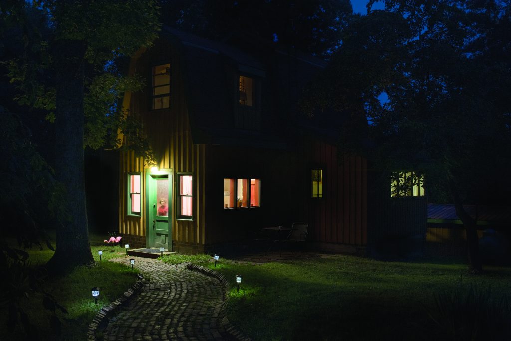 View of a quaint home in the woods at nighttime with a ghostly figure of a person standing in the door window