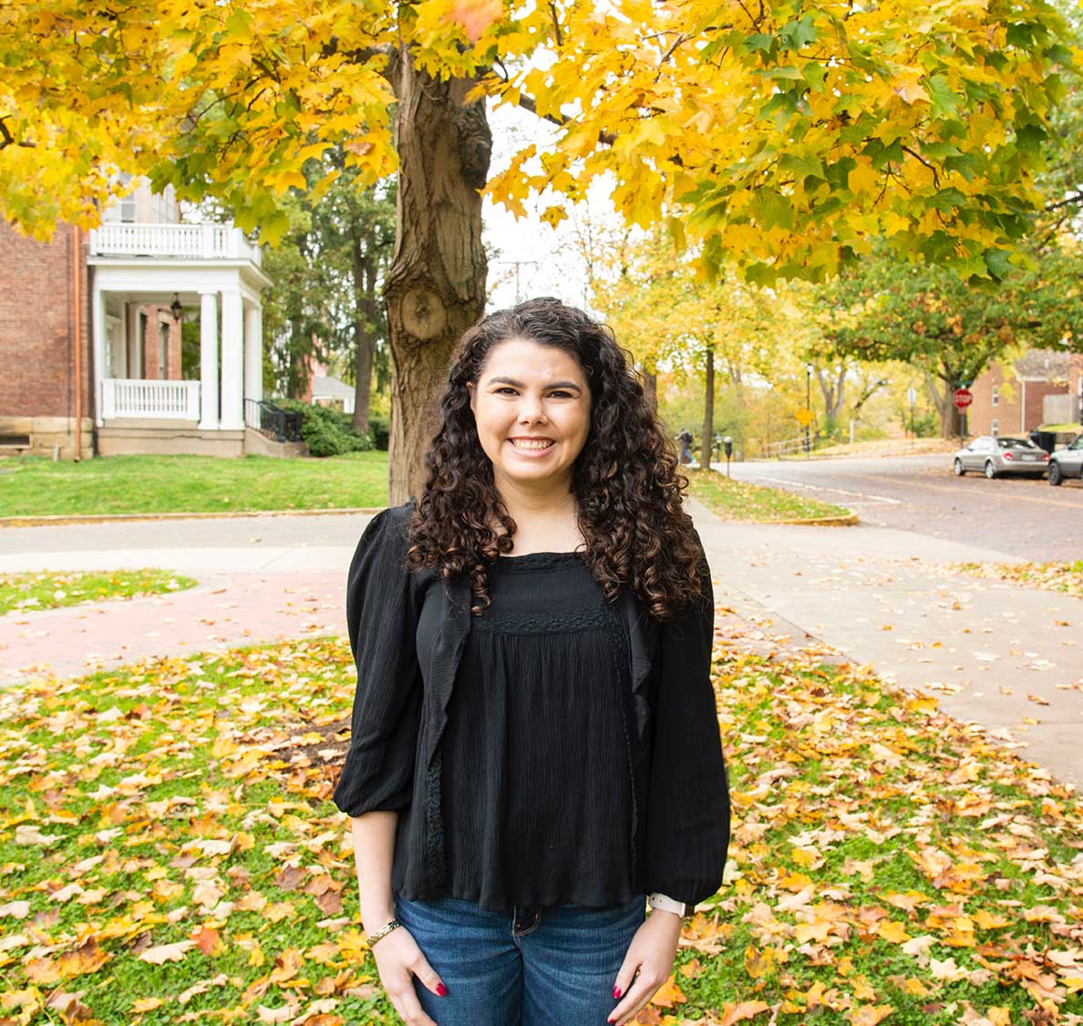 Caitlin Hunt, standing under brilliant yellow fall leaves 