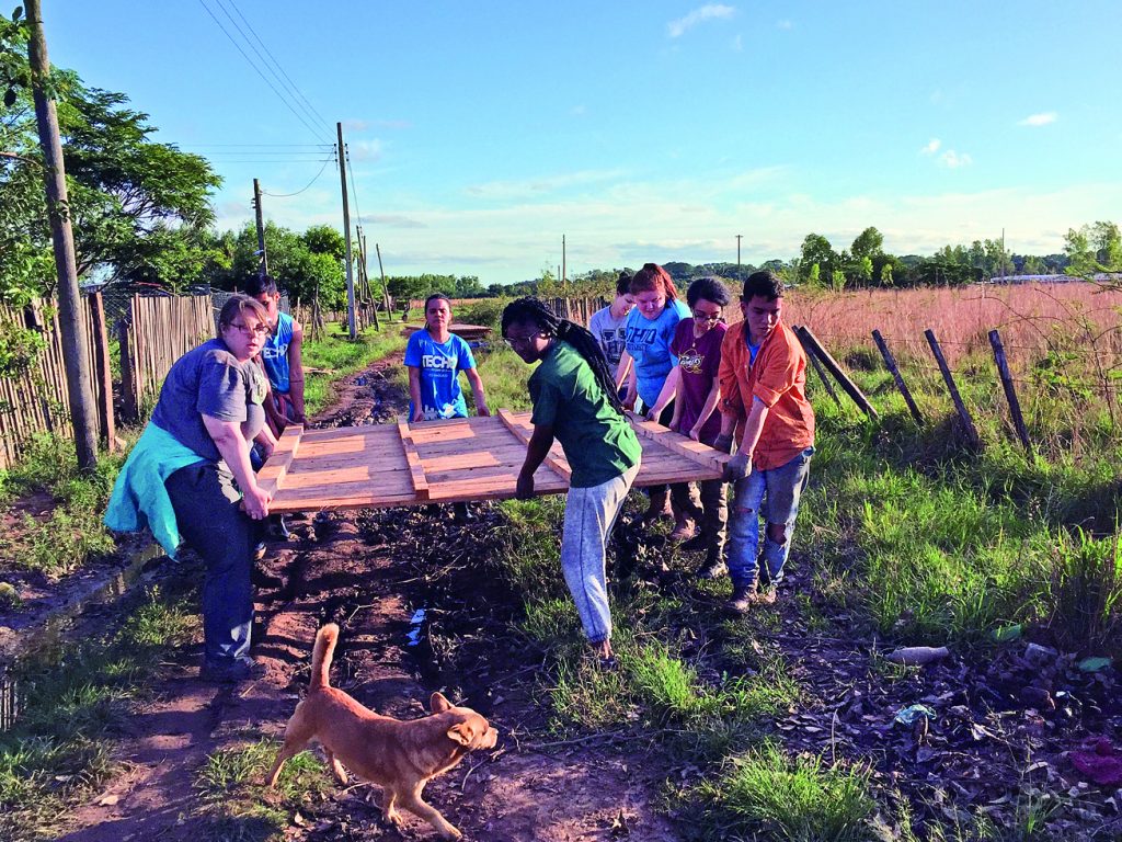 OHIO students and volunteers from TECHO, a nonprofit in Paraguay, team up to carry a panel wall that will become part of a home. Photo by Serena Verweire, CFS ’18