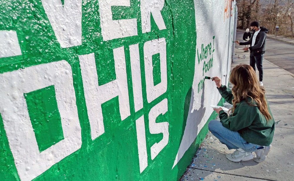 women painting OHIO's brand onto the graffiti wall.