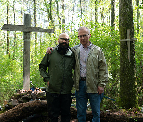 2 men standing in the woods in front of crosses on trees
